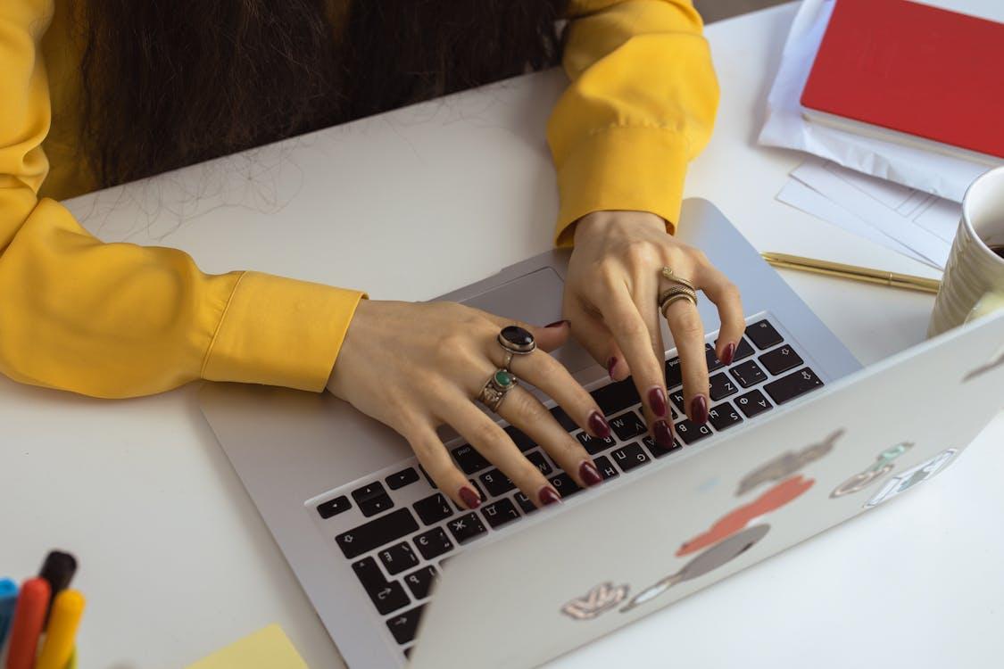 Free Woman in Yellow Long Sleeve Typing on Laptop Stock Photo