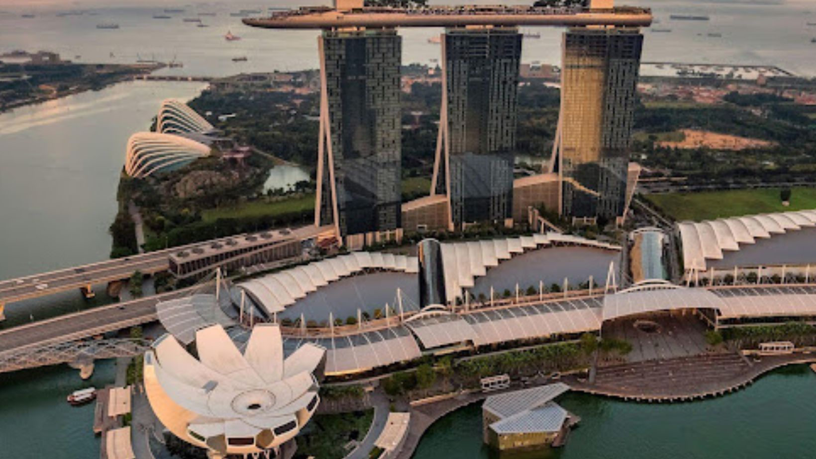 Aerial view of Marina Bay Sands with its three towers and rooftop SkyPark at sunset.